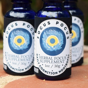 May include: Three blue glass bottles with droppers, each labeled "FOCUS POCUS" in a black circle with a yellow sun and blue leaves. The label also reads "HERBAL FOCUS SUPPLEMENT 1 oz / 30g DAILY COGNITION NOOTROPIC".