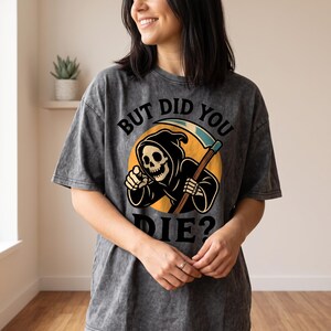 May include: A charcoal grey acid-wash t-shirt featuring a graphic of a grim reaper holding a scythe against a yellow circle. The text above reads BUT DID YOU and the text below reads DIE? The grim reaper is pointing forward with one hand.
