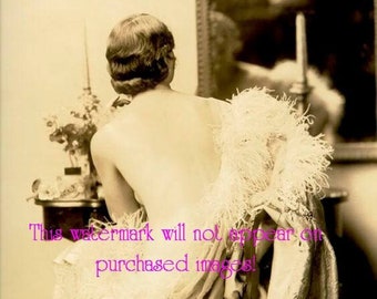 May include: A woman in a vintage photo sits in a chair, facing away from the camera. She is wearing a white feathered boa and a long, flowing gown. The photo is in black and white and has a faded, antique look.