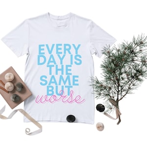 Puede incluir: Camiseta blanca con el texto "EVERY DAY IS THE SAME BUT WORSE" en letras azules y rosas.