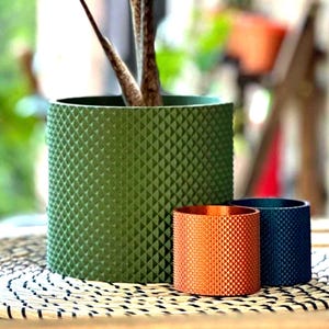 May include: Three geometric patterned plant pots in different sizes. The largest pot is green, the middle pot is orange, and the smallest pot is blue.