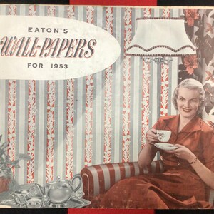 May include: Vintage Eaton's Wall-Papers catalogue cover from 1953. The cover shows a woman in a red dress holding a teacup, seated in a striped chair. The background displays wallpaper samples with red and white stripes.