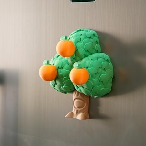 May include: A whimsical refrigerator magnet shaped like a tree with three orange fruits. The tree has a brown trunk and vibrant green leaves. The oranges have a textured appearance, adding a playful touch to this decorative item.