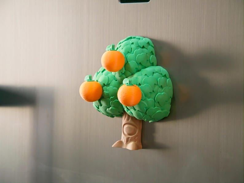 May include: A whimsical refrigerator magnet shaped like a tree with three orange fruits. The tree has a brown trunk and vibrant green leaves. The oranges have a textured appearance, adding a playful touch to this decorative item.