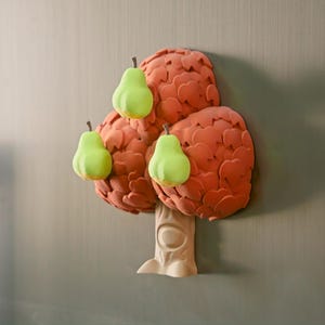 May include: A whimsical, three-dimensional tree sculpture with a light beige trunk and a textured, reddish-orange crown. Three bright green pears with brown stems are attached to the crown, creating a playful, nature-inspired design.