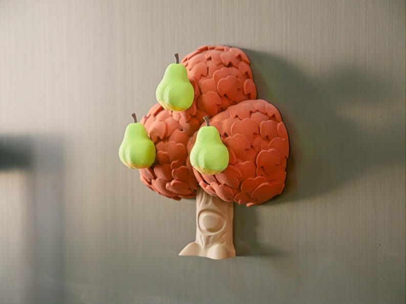 May include: A whimsical, three-dimensional tree sculpture with a light beige trunk and a textured, reddish-orange crown. Three bright green pears with brown stems are attached to the crown, creating a playful, nature-inspired design.