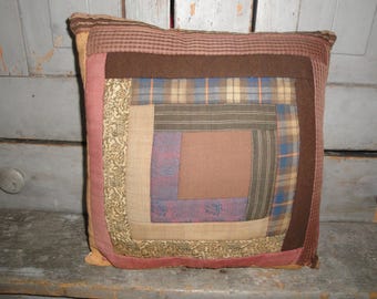 May include: A brown, tan, and blue patchwork pillow with a log cabin pattern. The pillow is made of different fabrics and has a rustic look.