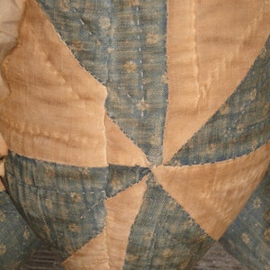 May include: A close-up of a handmade quilt with a starburst pattern. The quilt is made of blue and tan fabric and is stitched together with a running stitch. The quilt is worn and faded, suggesting it is an antique.
