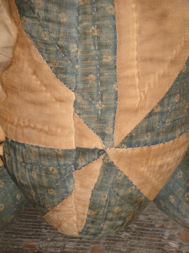May include: A close-up of a handmade quilt with a starburst pattern. The quilt is made of blue and tan fabric and is stitched together with a running stitch. The quilt is worn and faded, suggesting it is an antique.