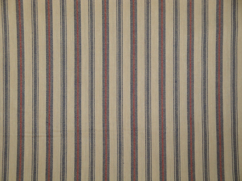 May include: A cream-coloured fabric featuring vertical stripes. Navy blue and red stripes alternate, running parallel. The fabric has a textured appearance, possibly woven, suitable for home decor or clothing.