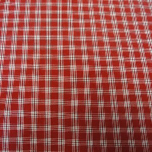 May include: Close-up of a red and white plaid fabric. The pattern consists of a grid of white lines intersecting over a red background, creating a classic checkered design. The fabric appears to be cotton or a similar woven material.