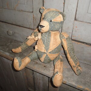 May include: A vintage patchwork teddy bear with a blue and tan color scheme. The bear is sitting on a wooden surface.