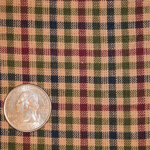 May include: A close-up of a tan, green, red, and black plaid fabric with a US quarter on top of it.