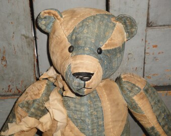 May include: A patchwork teddy bear with a blue and tan fabric design. The bear has black button eyes and a black stitched nose.