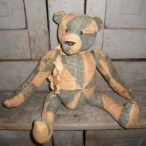 May include: A vintage patchwork teddy bear with a blue and tan patterned fabric. The bear is sitting on a wooden surface.