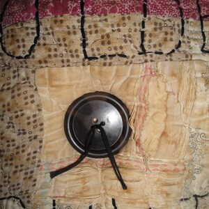 May include: A close-up of a vintage quilt with a brown button and black thread. The quilt is made of different fabrics and has a patchwork design. The word "OLD" is stitched in black thread on the quilt.