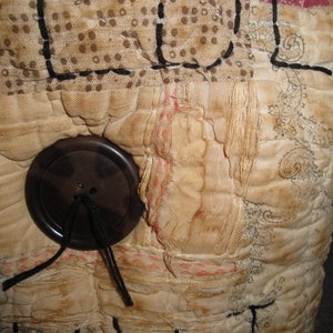 May include: A close-up of a vintage quilt with a brown button and black thread. The quilt is made of different fabrics and has a patchwork design.