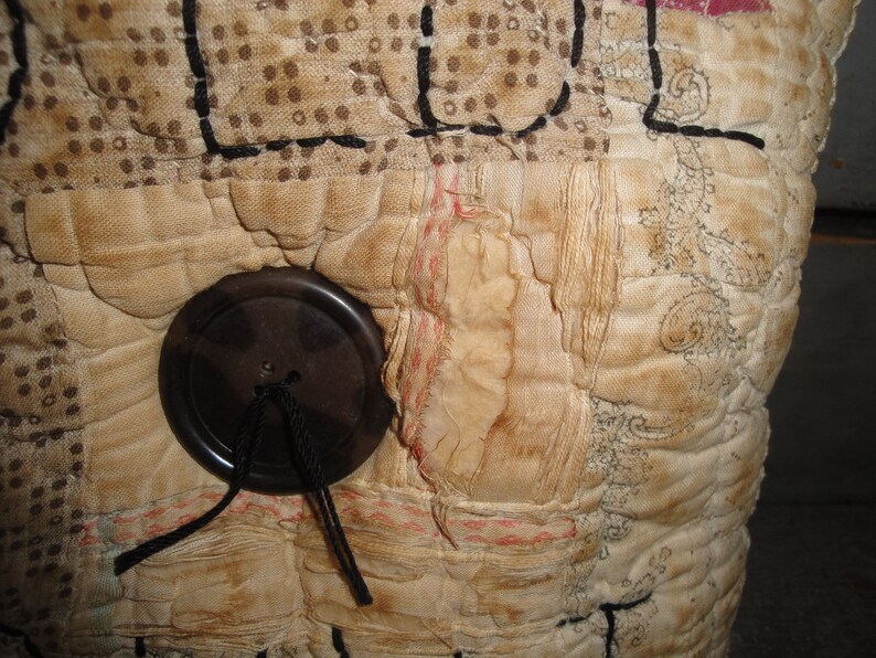 May include: A close-up of a vintage quilt with a brown button and black thread. The quilt is made of different fabrics and has a patchwork design.