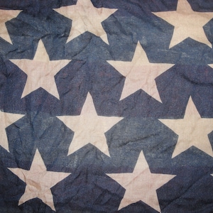 Op de afbeelding: Een close-up van een Amerikaanse vlag in blauw en wit met witte sterren op een blauwe achtergrond. De vlag is gemaakt van een textuurdoek en heeft een licht vervaagde uitstraling.