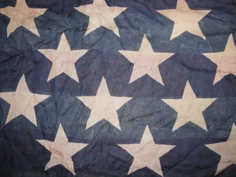 Op de afbeelding: Een close-up van een Amerikaanse vlag in blauw en wit met witte sterren op een blauwe achtergrond. De vlag is gemaakt van een textuurdoek en heeft een licht vervaagde uitstraling.