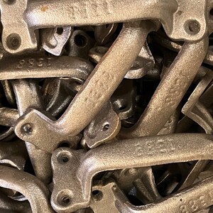 May include: A pile of cast iron door handles in a bronze finish. The handles are all in the same style, with a simple, curved design. They are stacked on top of each other, creating a textured and industrial look.