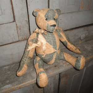 May include: A patchwork teddy bear with a blue and brown color scheme. The bear is sitting on a wooden surface.