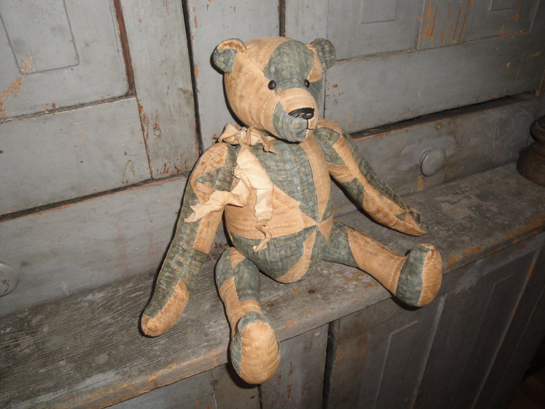 May include: A patchwork teddy bear with a blue and brown color scheme. The bear is sitting on a wooden surface.
