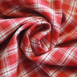 May include: Close-up of red and white plaid fabric, tightly swirled. The fabric has a classic checkered pattern with white lines on a red background. The fabric is folded and draped, creating a textured effect.