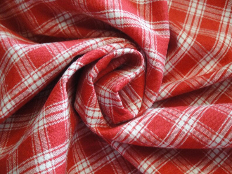 May include: Close-up of red and white plaid fabric, tightly swirled. The fabric has a classic checkered pattern with white lines on a red background. The fabric is folded and draped, creating a textured effect.