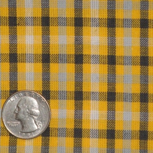 May include: Yellow and black plaid fabric with a quarter on top of it.