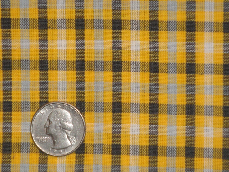 May include: Yellow and black plaid fabric with a quarter on top of it.