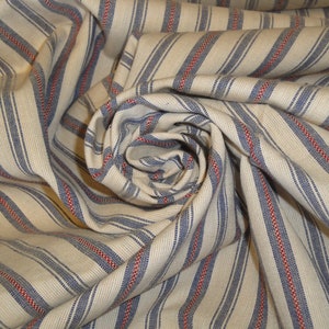 May include: A close-up of a fabric with a cream background and vertical stripes. The stripes alternate between blue and red, creating a classic, textured pattern. The fabric is gathered and folded, showing the texture and drape of the material.