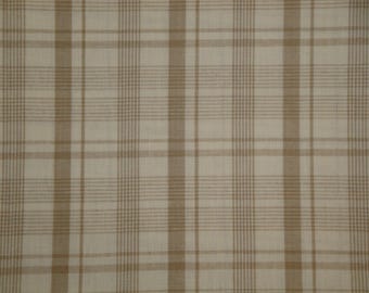 May include: Close-up of a beige and brown plaid fabric. The pattern consists of vertical and horizontal lines creating a grid-like design. The fabric has a textured appearance, with a mix of light and dark brown hues.