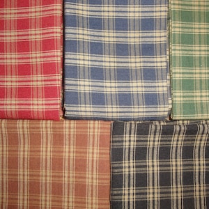 May include: Close-up of five fabric swatches in a plaid pattern. The colors include red, blue, green, brown, and navy. Each swatch has a cream-colored grid pattern overlaying the base color. The fabric appears to be cotton or a similar material.