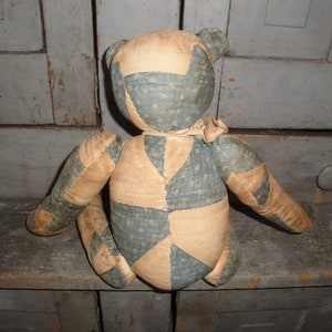 May include: A patchwork teddy bear made from blue and tan fabric. The bear is sitting on a wooden surface.
