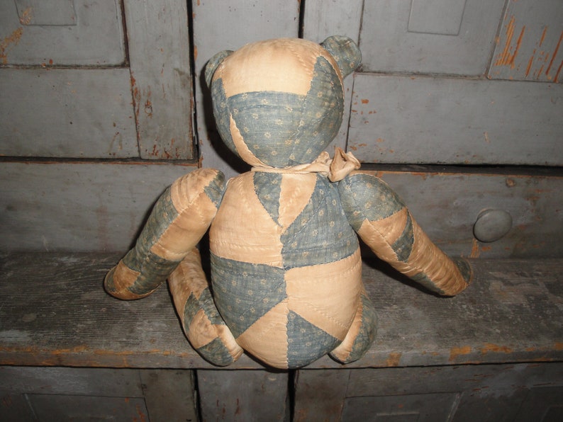 May include: A patchwork teddy bear made from blue and tan fabric. The bear is sitting on a wooden surface.