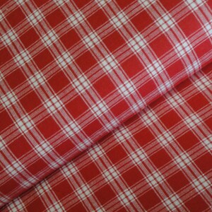 May include: Close-up of red and white plaid fabric. The fabric features a classic plaid pattern with intersecting white lines on a red background. The fabric is folded, showing the texture and drape of the material.
