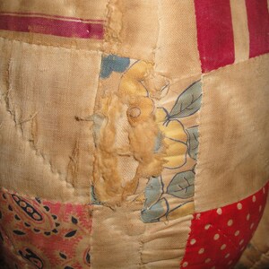 May include: A patchwork quilt with a variety of fabrics, including floral prints, stripes, and paisley patterns. The quilt is made of different shades of brown, red, and white.