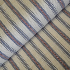 May include: Cream-coloured fabric featuring a repeating pattern of blue and red stripes. The stripes run diagonally across the fabric, creating a visually interesting texture. The fabric appears to be folded over itself.