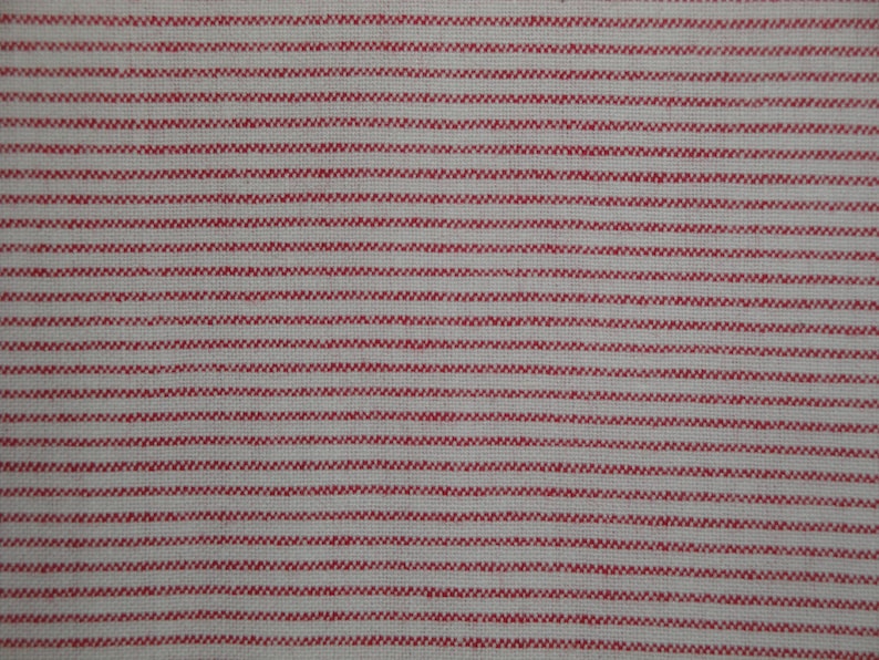 May include: Close-up of a fabric with a repeating pattern of thin, horizontal red stripes on a white background. The stripes have a textured, zig-zag appearance, creating a visually interesting design. The fabric appears to be a woven material, possibly cotton or linen.