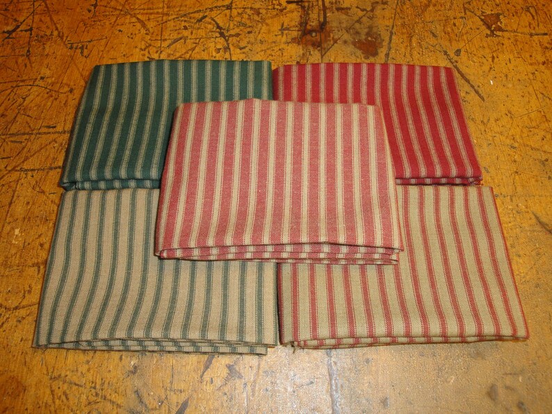 May include: Six fabric squares with a striped pattern. The squares are folded in half and stacked on top of each other. The stripes are red and tan, green and tan, and red and tan.