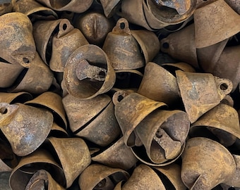 May include: A pile of antique, rusty metal bells. The bells are various sizes and shapes, with a loop at the top for hanging and a clapper inside. The overall color is a mix of brown and gold, with signs of age and wear.