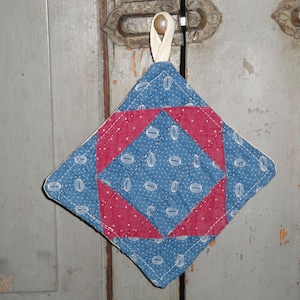 May include: A blue and red quilted pot holder with a diamond shape and white polka dots. The pot holder has a loop for hanging.