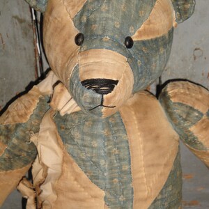 May include: A vintage patchwork teddy bear with a blue and tan fabric design. The bear has black button eyes and a black stitched nose.