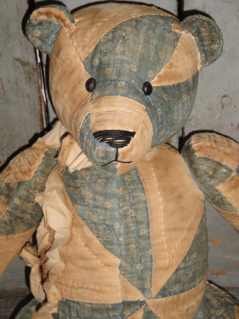 May include: A vintage patchwork teddy bear with a blue and tan fabric design. The bear has black button eyes and a black stitched nose.
