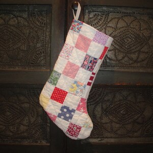May include: A white patchwork Christmas stocking with red, blue, and green squares. The stocking is hanging on a dark wooden door.