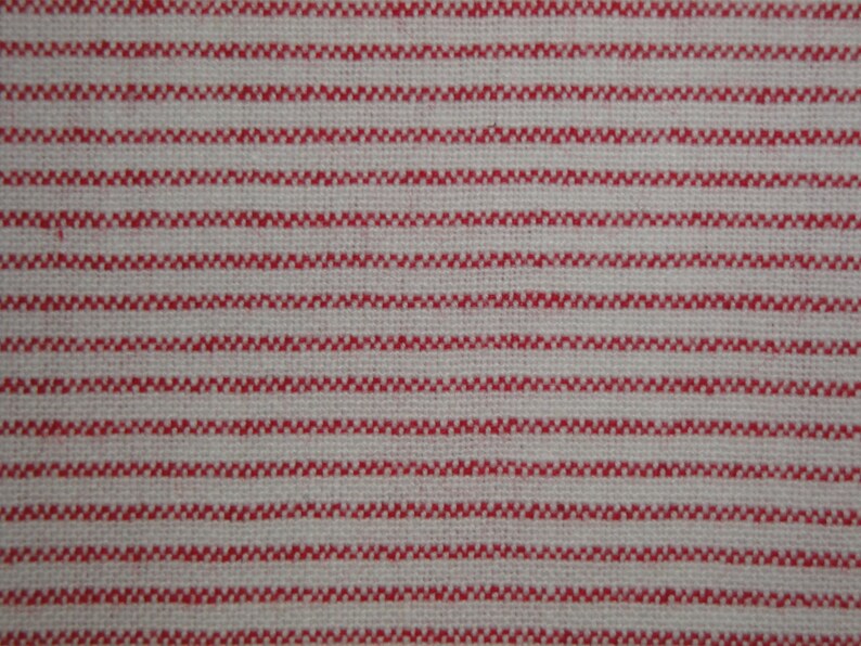 May include: Close-up of a woven fabric with a repeating pattern of horizontal red stripes on a cream-colored background. The stripes have a textured, zig-zag appearance, creating a visually interesting textile.