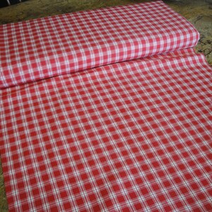 May include: A roll of red and white checkered fabric. The fabric is unrolled, revealing a large surface area of the pattern. The pattern is a classic gingham design, with evenly spaced red and white squares. The fabric is likely cotton or a similar material.