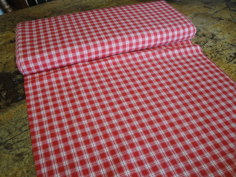 May include: A roll of red and white checkered fabric. The fabric is unrolled, revealing a large surface area of the pattern. The pattern is a classic gingham design, with evenly spaced red and white squares. The fabric is likely cotton or a similar material.