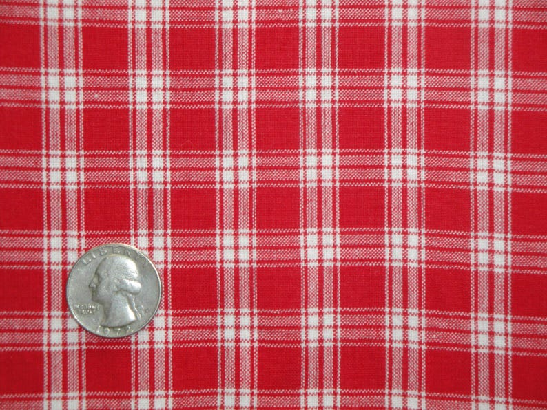 May include: Close-up of red and white plaid fabric. The fabric has a classic checkered pattern with a quarter coin for size reference. The fabric is likely cotton or a similar material.